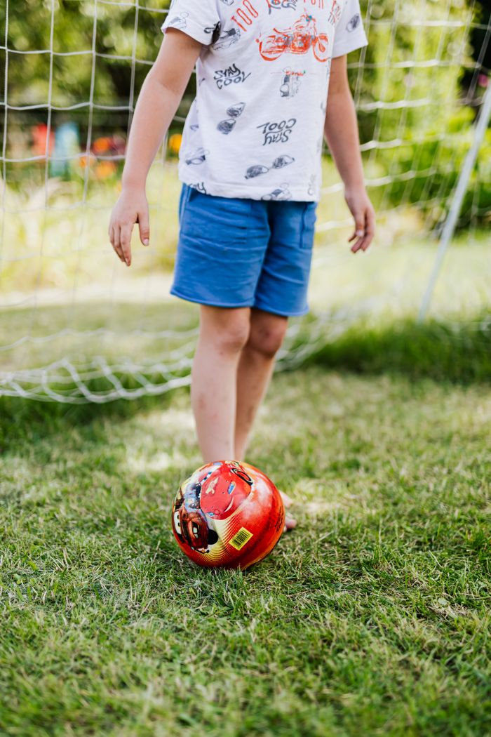 A child playing soccer in a sunny backyard with green grass.